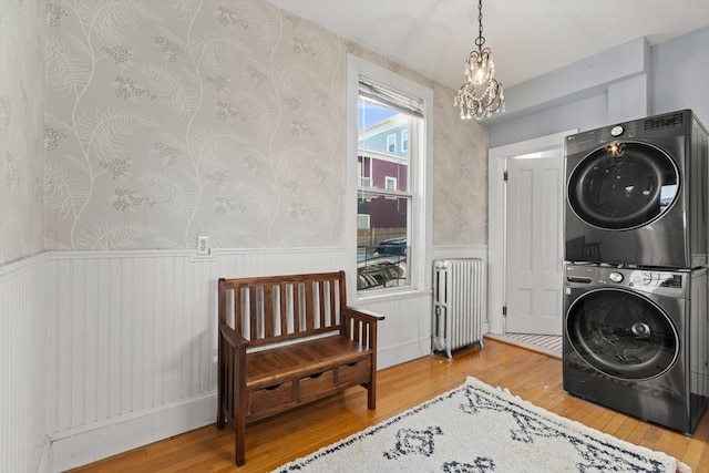 clothes washing area with a wainscoted wall, stacked washer and dryer, laundry area, radiator, and wallpapered walls