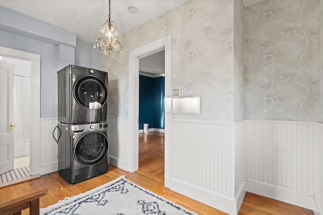 washroom featuring stacked washing maching and dryer, laundry area, wallpapered walls, and wainscoting