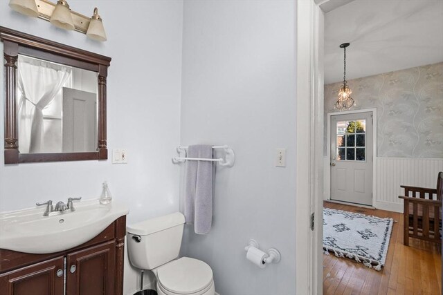 bathroom with wallpapered walls, toilet, hardwood / wood-style flooring, a wainscoted wall, and vanity