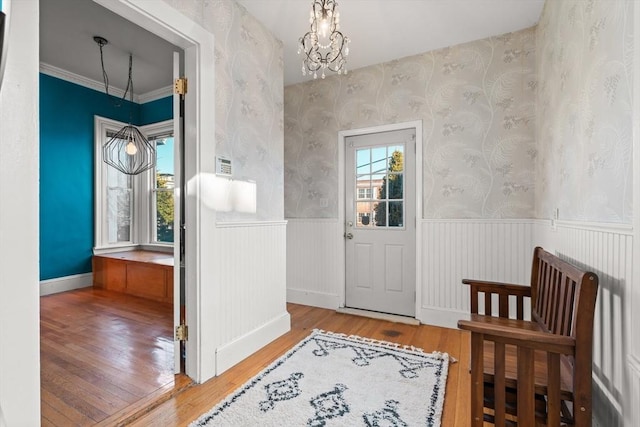 foyer entrance with wallpapered walls, a wainscoted wall, wood-type flooring, ornamental molding, and a chandelier