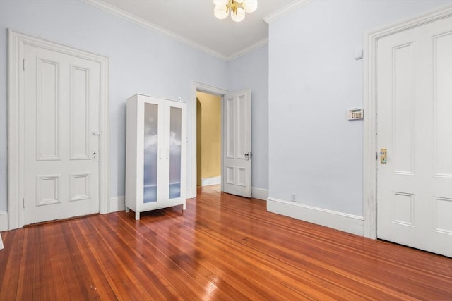 unfurnished bedroom featuring a chandelier, crown molding, baseboards, and wood finished floors