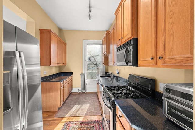 kitchen with a toaster, dark stone counters, appliances with stainless steel finishes, rail lighting, and light wood-style floors