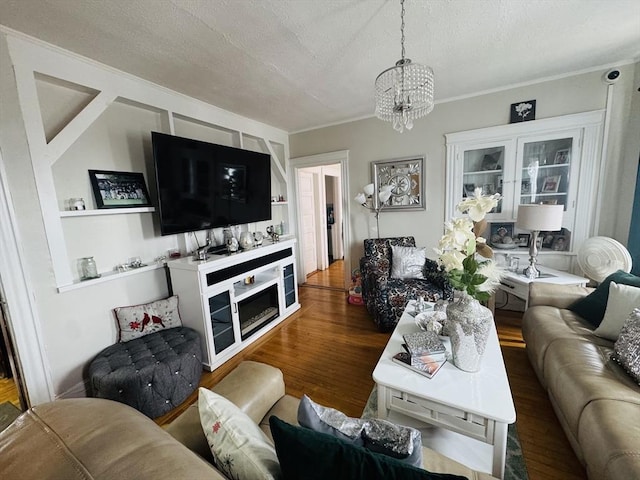 living room with a chandelier, a textured ceiling, wood finished floors, and ornamental molding