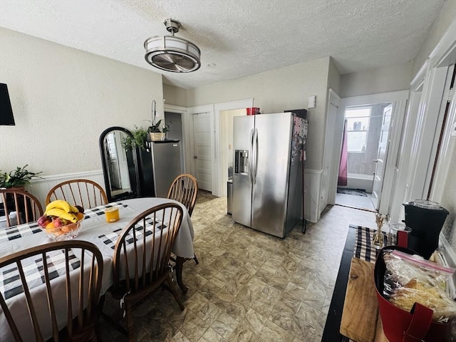 kitchen with a textured wall, stainless steel fridge, light floors, and a textured ceiling