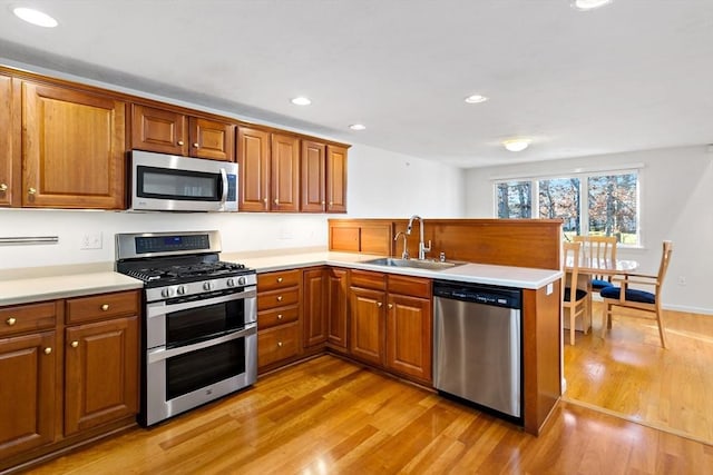 kitchen with kitchen peninsula, sink, stainless steel appliances, and light hardwood / wood-style flooring