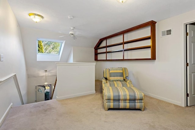 sitting room featuring ceiling fan, vaulted ceiling with skylight, and light colored carpet