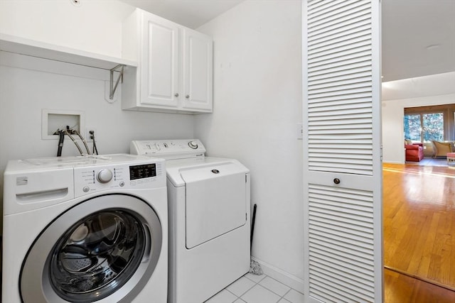 clothes washing area with light tile patterned flooring, cabinets, and washing machine and dryer