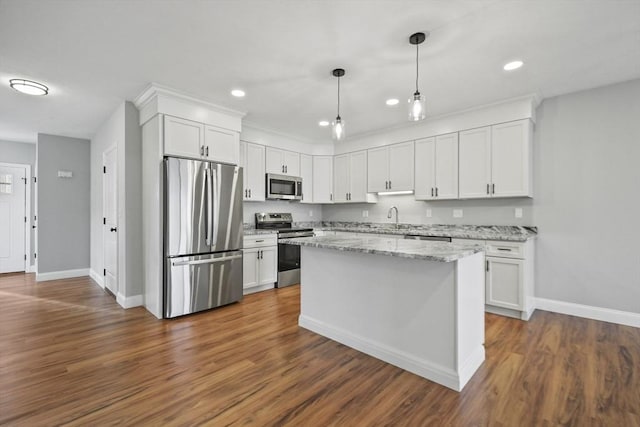 kitchen with pendant lighting, appliances with stainless steel finishes, white cabinetry, a center island, and light stone counters