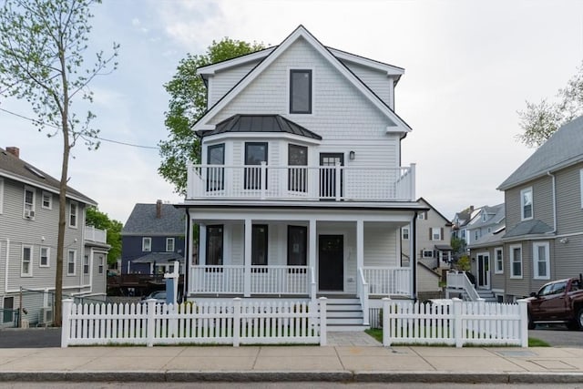 view of front of property with covered porch, a fenced front yard, a balcony, and a standing seam roof
