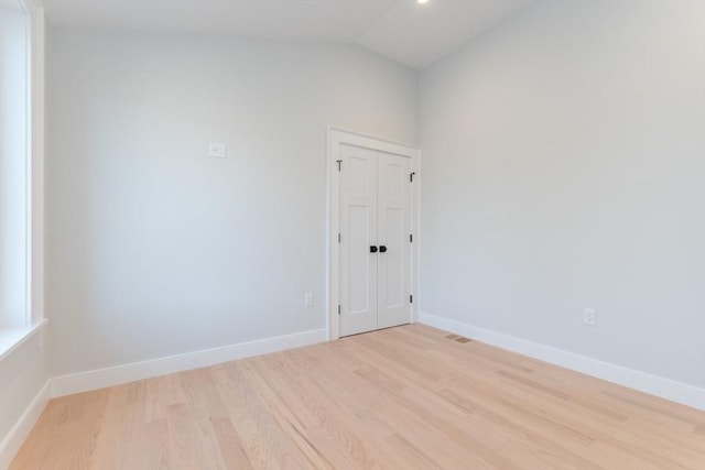 unfurnished room with light wood finished floors, vaulted ceiling, and baseboards