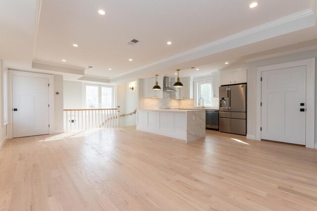 kitchen featuring stainless steel appliances, wall chimney exhaust hood, plenty of natural light, a raised ceiling, and crown molding