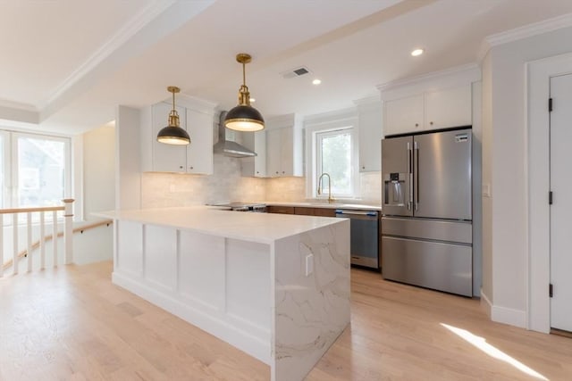 kitchen featuring appliances with stainless steel finishes, wall chimney range hood, light wood finished floors, decorative backsplash, and crown molding