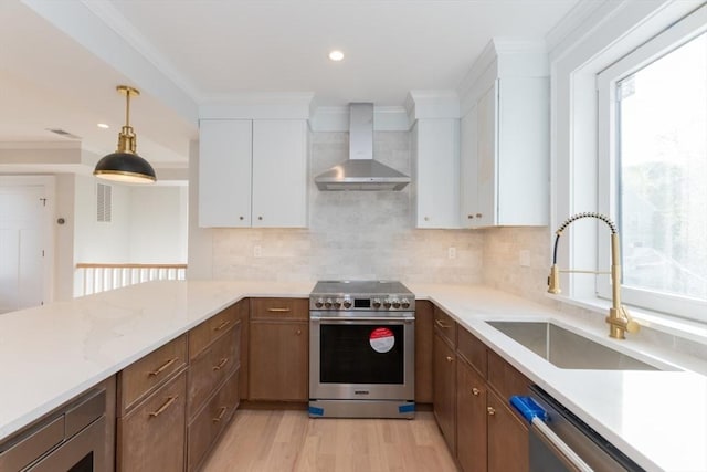 kitchen with wall chimney range hood, stainless steel appliances, a sink, backsplash, and white cabinets