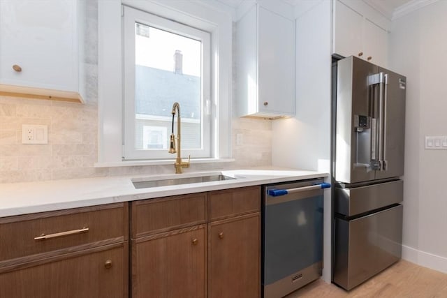 kitchen with appliances with stainless steel finishes, a sink, light countertops, tasteful backsplash, and crown molding