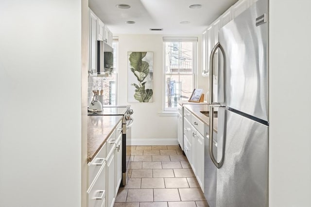 kitchen featuring light tile patterned floors, appliances with stainless steel finishes, white cabinetry, and light stone countertops