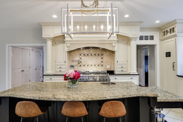 kitchen with backsplash, a large island with sink, a kitchen breakfast bar, sink, and light stone counters