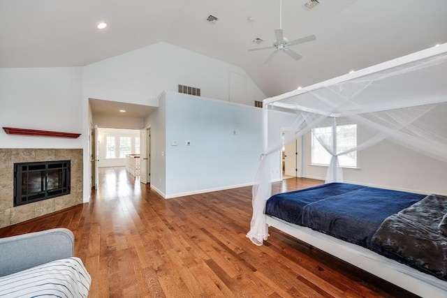 bedroom with ceiling fan, wood-type flooring, multiple windows, and a tiled fireplace