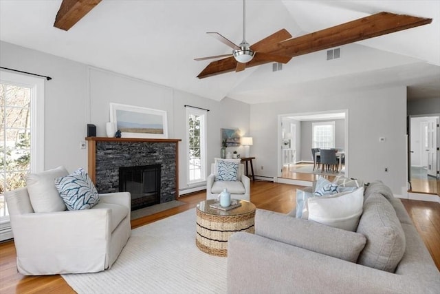 living room featuring a baseboard heating unit, lofted ceiling with beams, a healthy amount of sunlight, and light wood-type flooring