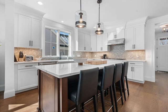 kitchen with white cabinets, a kitchen island, a breakfast bar area, dark wood-style flooring, and under cabinet range hood