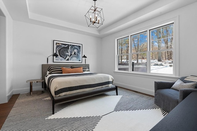 bedroom with a notable chandelier, a raised ceiling, wood finished floors, and baseboards