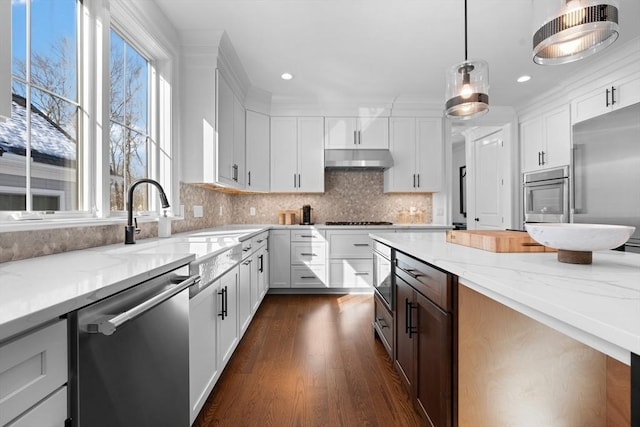 kitchen featuring appliances with stainless steel finishes, light stone countertops, under cabinet range hood, white cabinetry, and backsplash