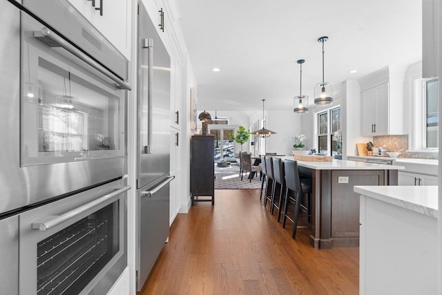 kitchen featuring dark wood-style floors, a kitchen island, stainless steel appliances, a kitchen bar, and white cabinetry