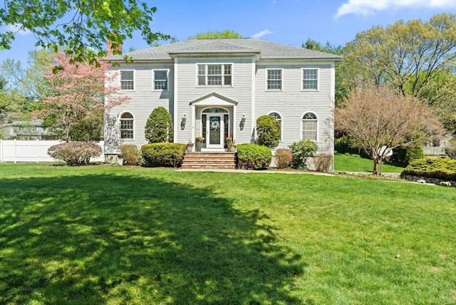 colonial home featuring a chimney, fence, and a front yard