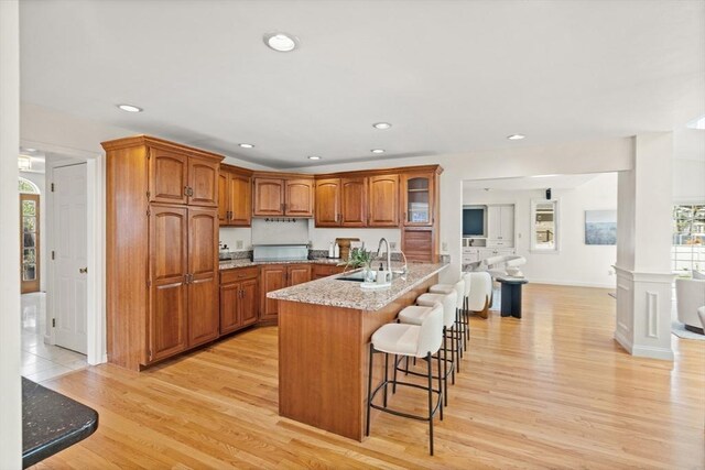 kitchen with brown cabinets, a breakfast bar, a sink, light wood finished floors, and a healthy amount of sunlight