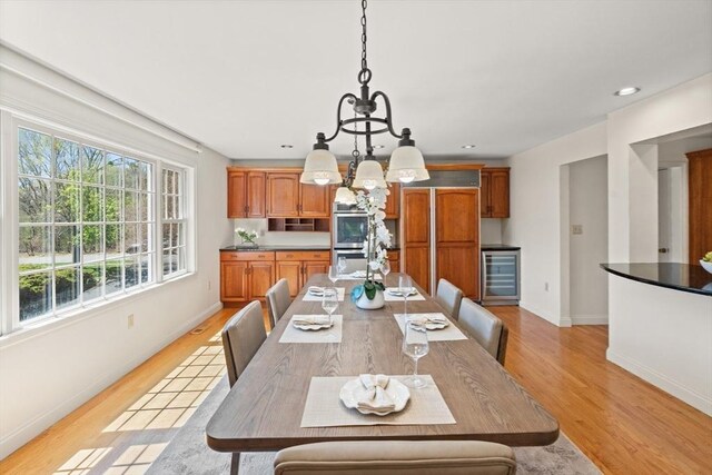 dining room with a healthy amount of sunlight, an inviting chandelier, light wood-type flooring, and beverage cooler
