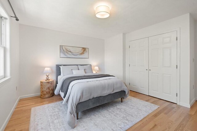 bedroom with light wood-type flooring, baseboards, and a closet