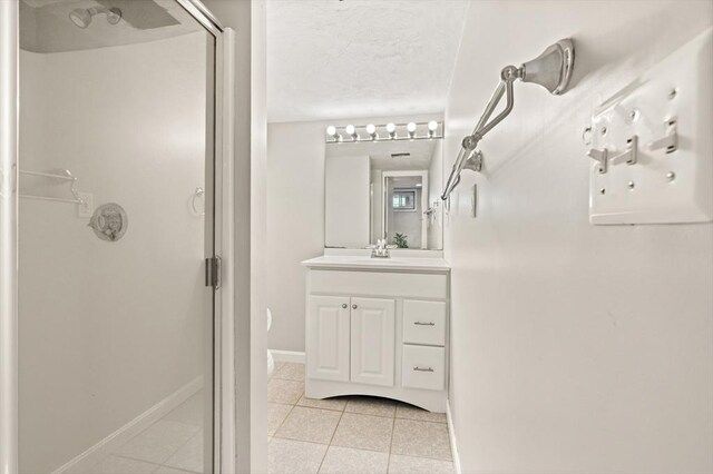 bathroom with vanity, baseboards, a textured ceiling, tile patterned floors, and a shower stall