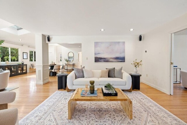 living room featuring light wood-style floors, baseboards, recessed lighting, and ornate columns