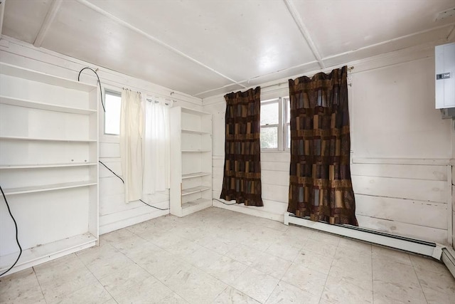 empty room with plenty of natural light, a baseboard heating unit, and wood walls