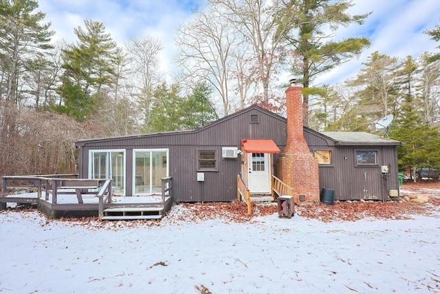 snow covered house with an AC wall unit and a deck