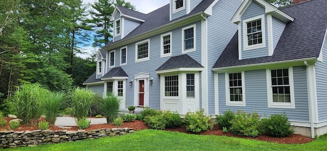 cape cod home with a shingled roof and a front lawn