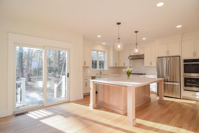 kitchen featuring stainless steel appliances, sink, a center island, white cabinetry, and pendant lighting