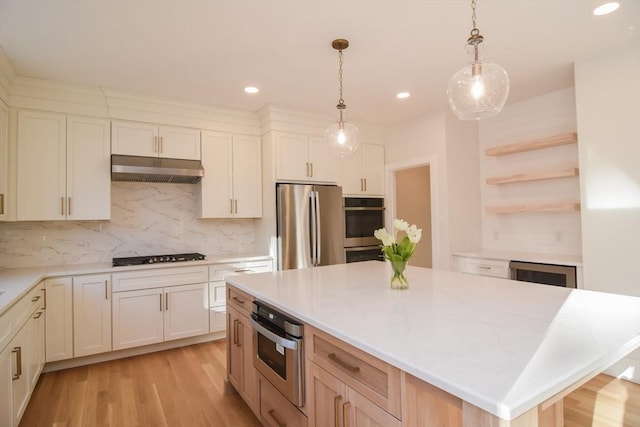 kitchen featuring appliances with stainless steel finishes, a center island, light hardwood / wood-style flooring, decorative light fixtures, and tasteful backsplash