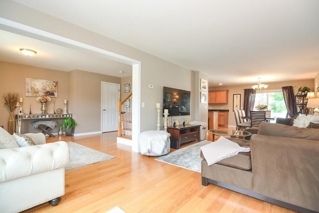 living room with a notable chandelier, baseboards, stairs, and light wood-style floors