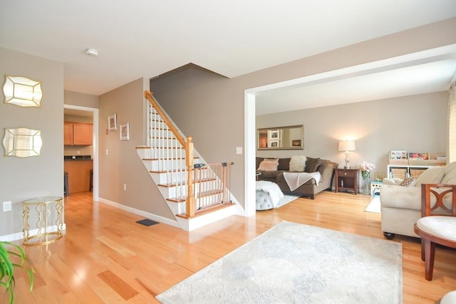 living room featuring visible vents, baseboards, light wood-style flooring, and stairs