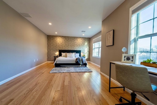 bedroom featuring light wood-type flooring, baseboards, visible vents, and an accent wall