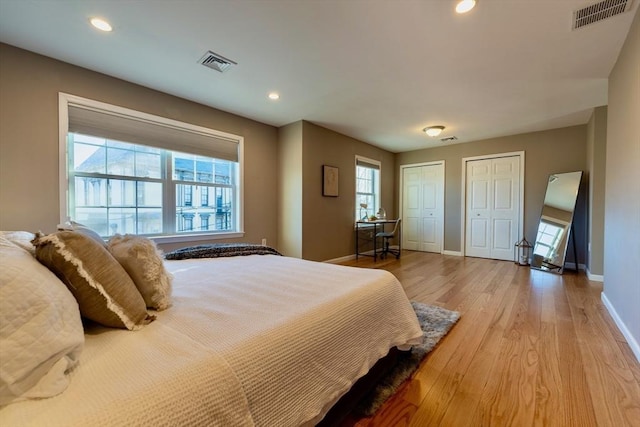 bedroom with visible vents, multiple closets, baseboards, and light wood finished floors