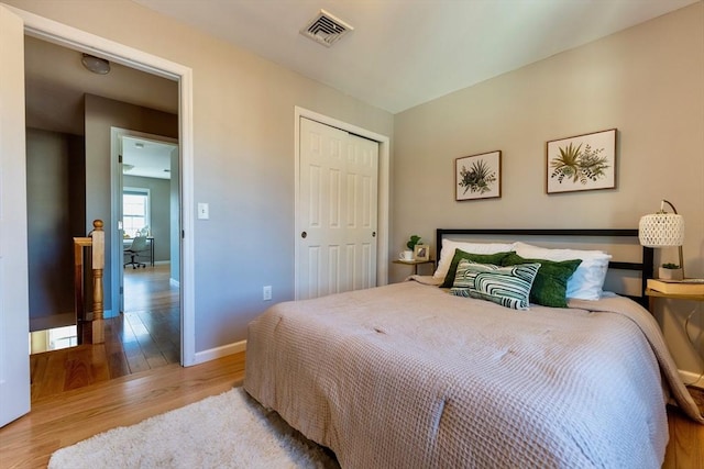 bedroom with wood finished floors, visible vents, a closet, and baseboards