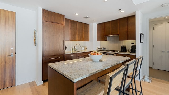 kitchen featuring light stone countertops, light hardwood / wood-style flooring, tasteful backsplash, a center island, and a breakfast bar area