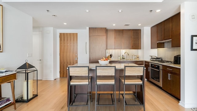 kitchen with light hardwood / wood-style flooring, backsplash, a kitchen breakfast bar, a center island, and appliances with stainless steel finishes