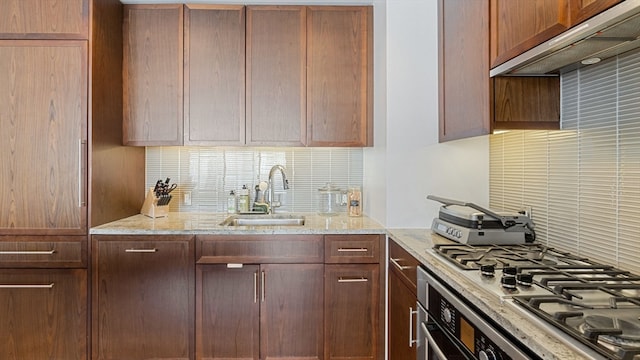 kitchen with light stone counters, backsplash, gas stovetop, sink, and premium range hood