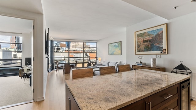 kitchen featuring dark brown cabinetry, wine cooler, light stone countertops, a center island, and light colored carpet