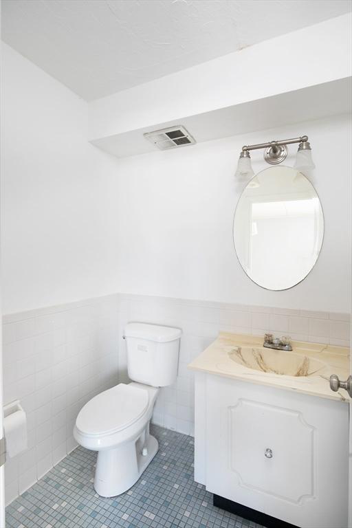 bathroom with toilet, wainscoting, tile walls, and vanity