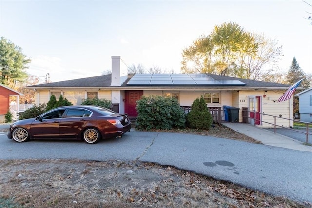 ranch-style home with a chimney, fence, and solar panels