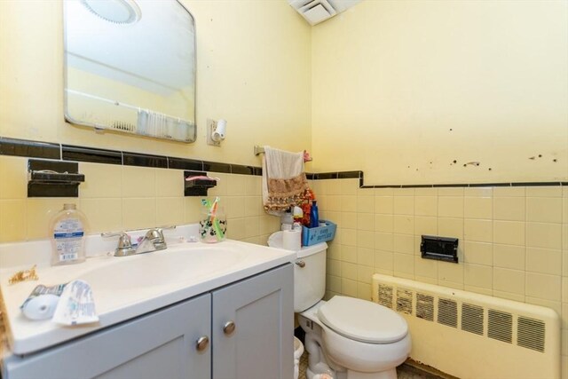 bathroom featuring toilet, visible vents, tile walls, vanity, and radiator