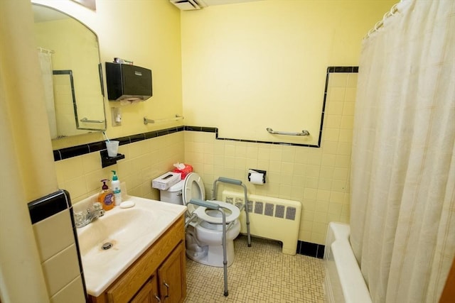 bathroom with tile patterned flooring, toilet, vanity, tile walls, and radiator heating unit